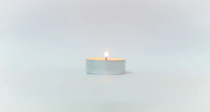 A minimalist white candle centered on a white background, featuring a small flame