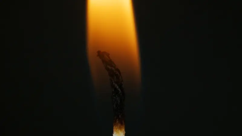Intimate close-up of a candle wick burning with a soft flame against a dark background