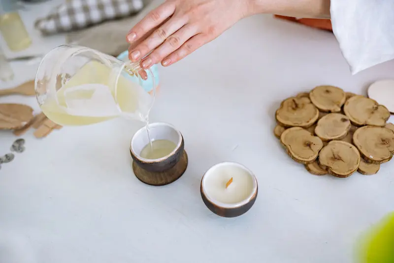 Close-up of hand pouring candle wax into rustic container, crafting essentials nearby