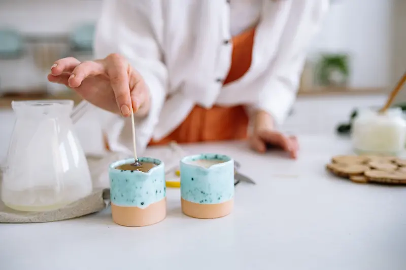 Close-up of hands making handmade candles using soy wax in decorative containers