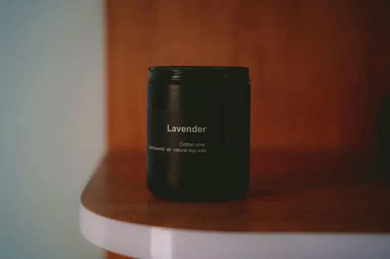 A lavender scented soy wax candle on a wooden shelf in soft light